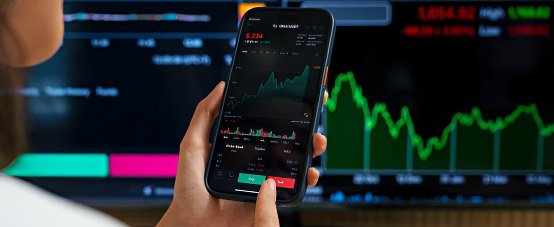 A person checking stock market data on a smartphone in front of a large display.